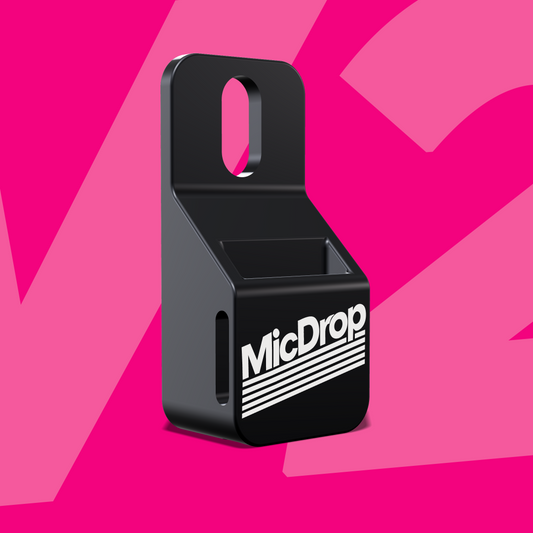 MicDrop V2 wireless mic mount in black anodized aluminum with a white MicDrop logo, standing upright on a pink background