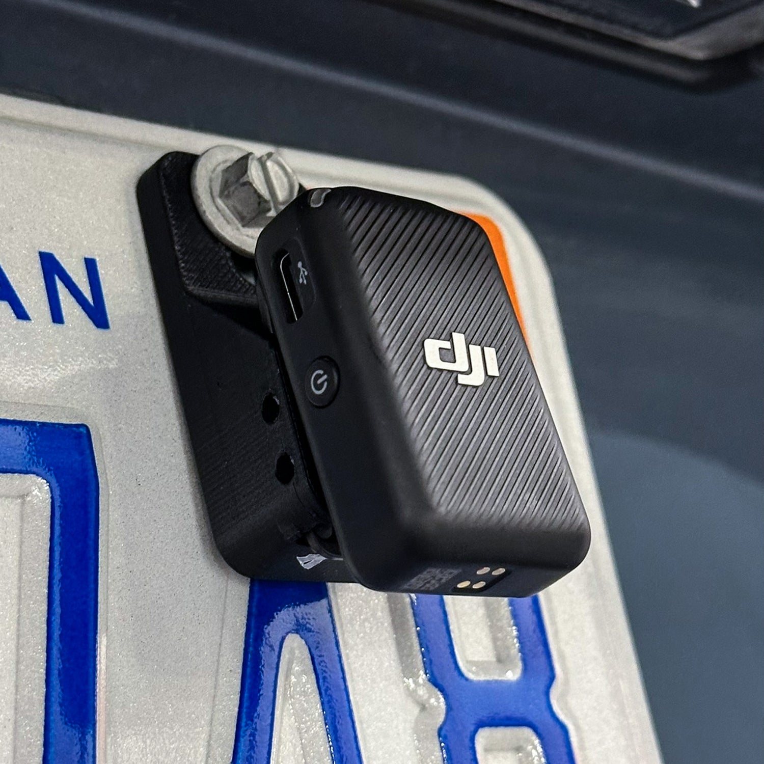 The MicDrop wireless mic mount securely attached to a car license plate, capturing high-quality exhaust audio without wind noise.