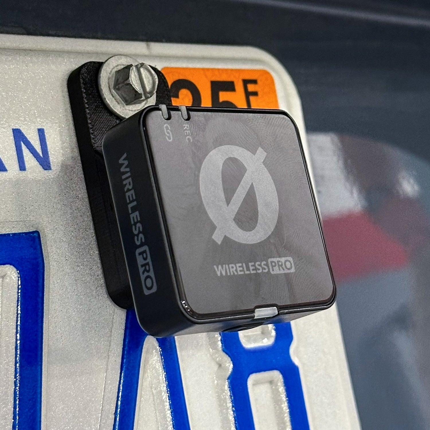 The MicDrop wireless mic mount securely attached to a car license plate, capturing high-quality exhaust audio without wind noise using a Rode Wireless Pro.